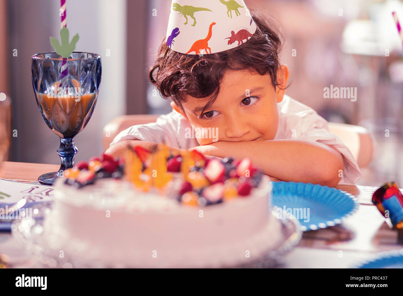 Dreamy boy thoughtfully looking at the cake while having birthday party Stock Photo