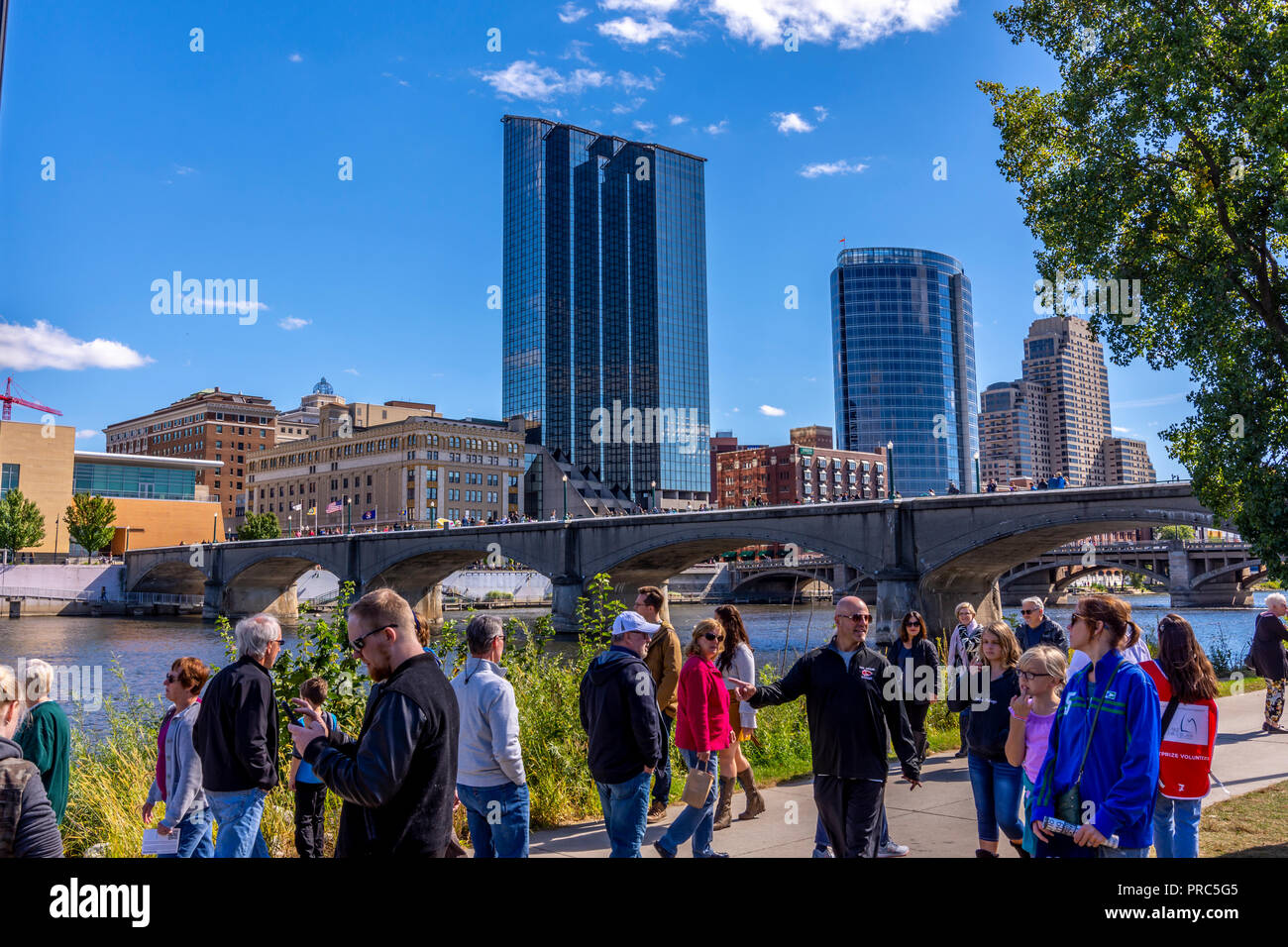 People stroll along the Grand River with Grand Rapids skyline and Pearl