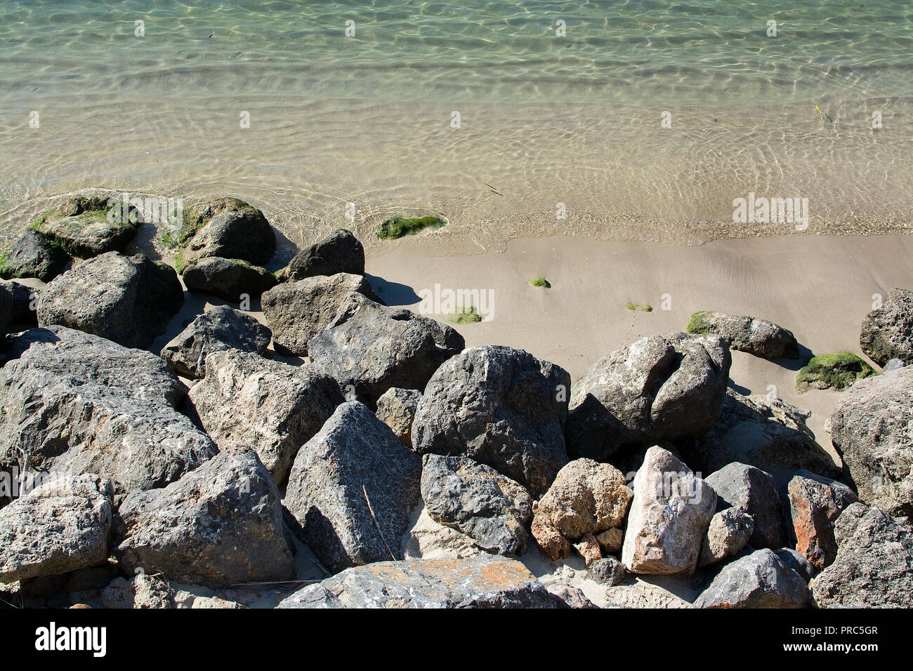 Rocks and shallow sand in green ocean water closeup on a sunny afternoon on a sunny day in Mallorca, Spain. Stock Photo