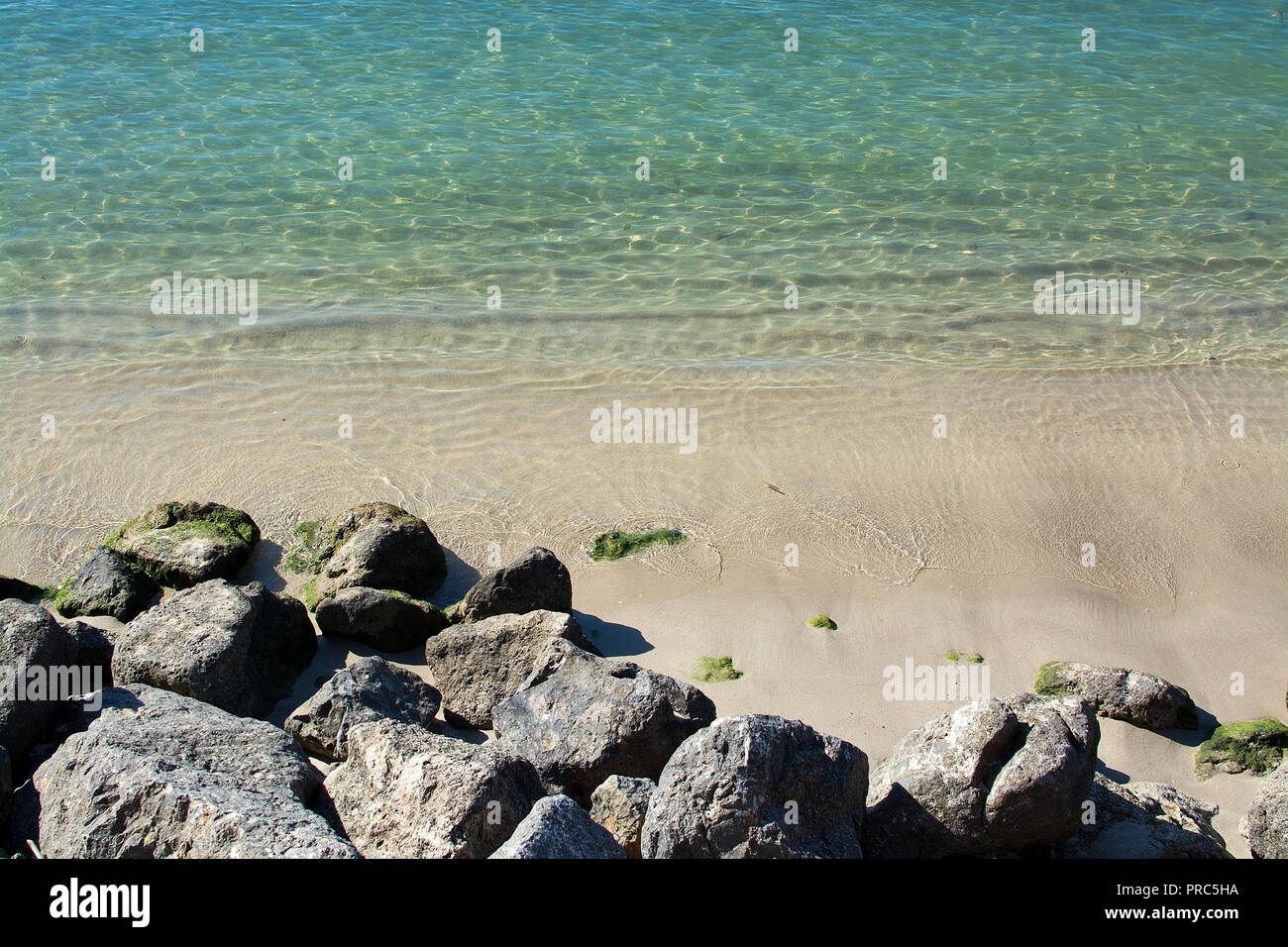 Rocks and shallow sand in ocean water closeup on a sunny afternoon on a sunny day in Mallorca, Spain. Stock Photo