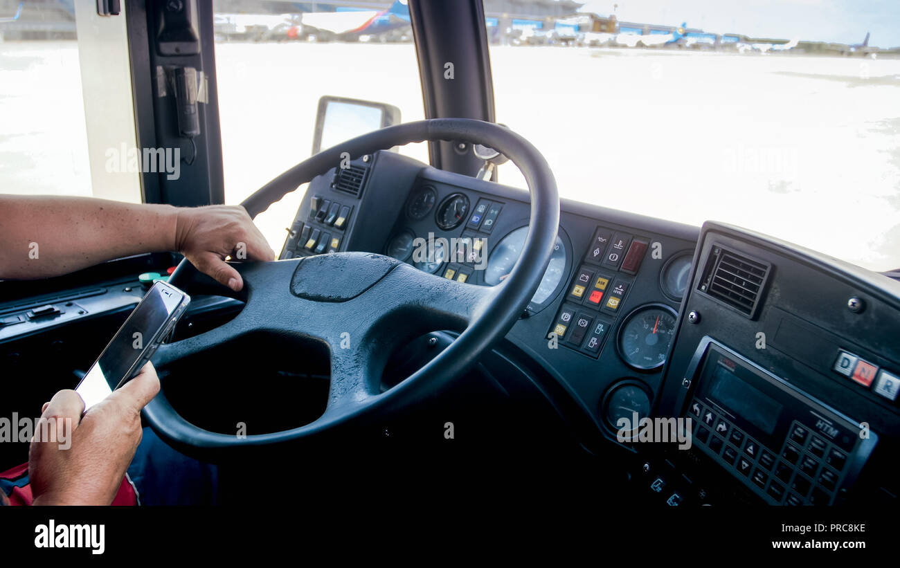 Closeup photo of irresponsible driver using smartphone while driving bus on airport runway Stock Photo