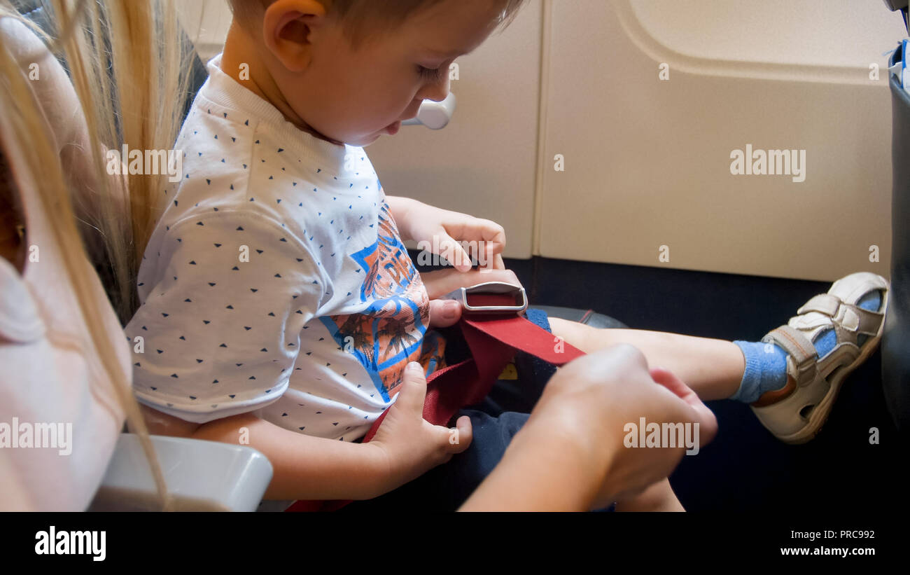Mother fastening and pulling safety seat belt of her child in aircraft before taking off Stock