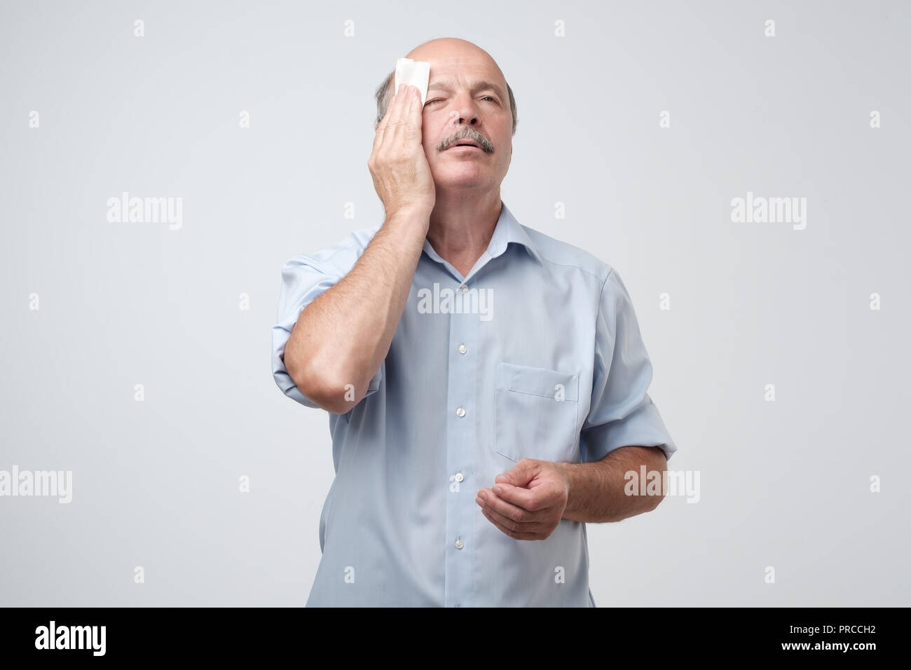 Tired old man with mustache stressed sweating having fever headache isolated on gray wall background. Worried guy wipes sweat on his face Stock Photo