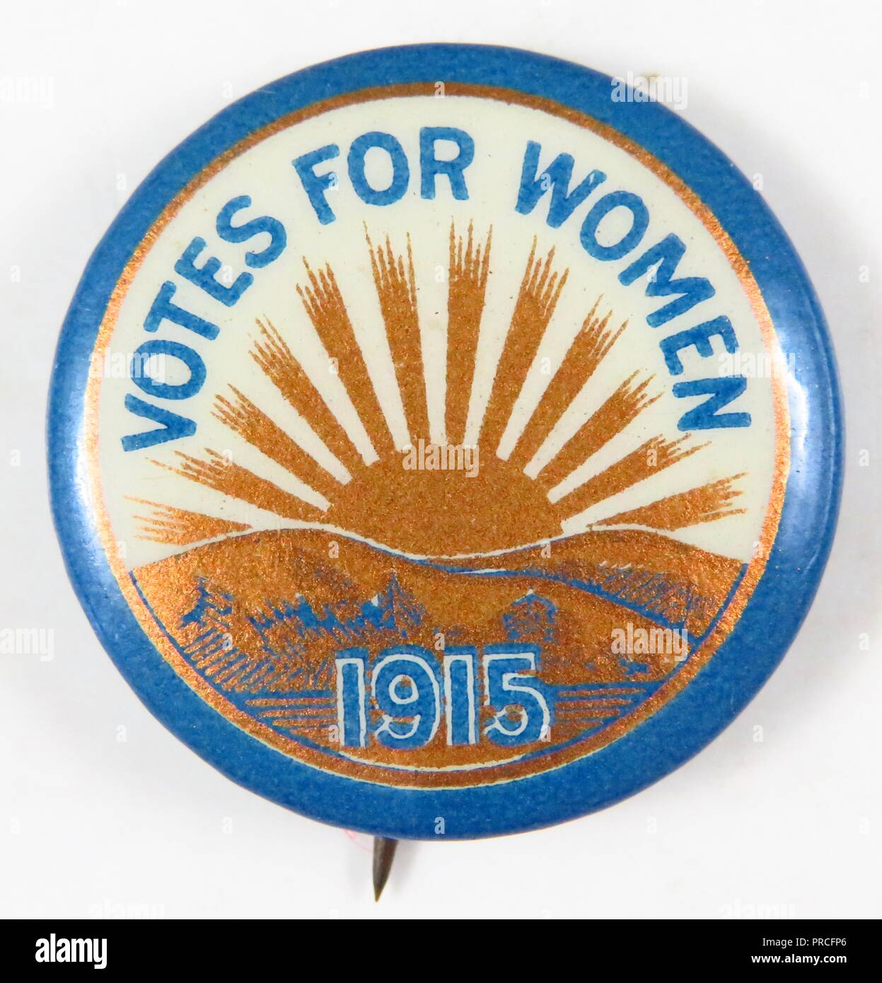 Orange and blue suffrage pin, designed using the unofficial colors of New York State, with an image of the sun rising over rolling hills, and the text aVotes for Women 1915, manufactured for the American market, to promote the contemporaneous Empire State Campaign, 1915. Photography by Emilia van Beugen. () Stock Photo