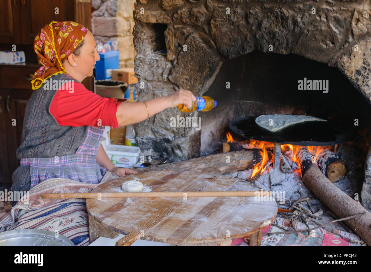 A Turkish woman makes traditional Turkish flatbread (balloon bread) over a log fire and griddle, Turkey. Stock Photo