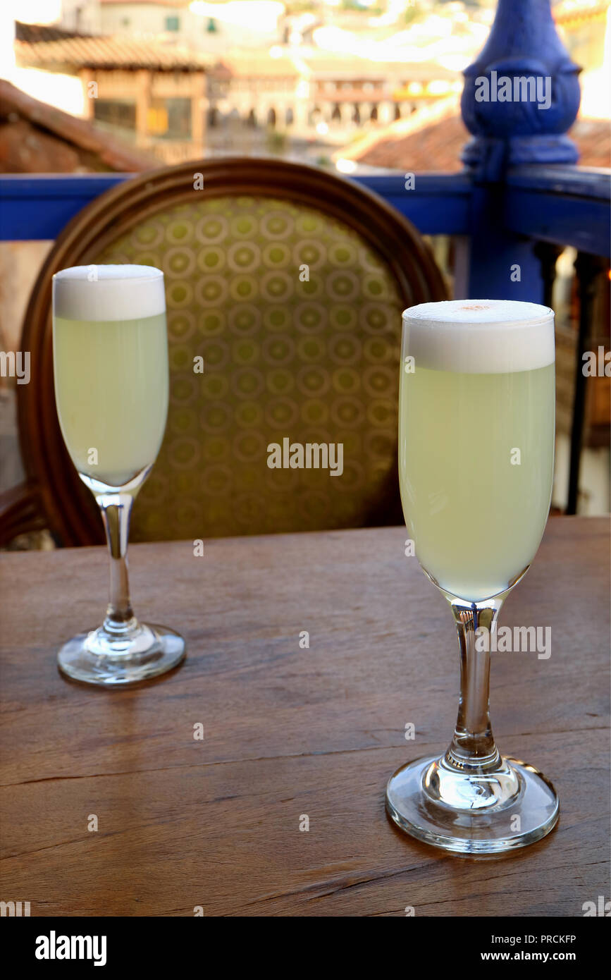 Two glass of Peruvian Pisco Sour on wooden table with a vintage chair and  blurred building in background, old town of Cusco, Peru Stock Photo - Alamy