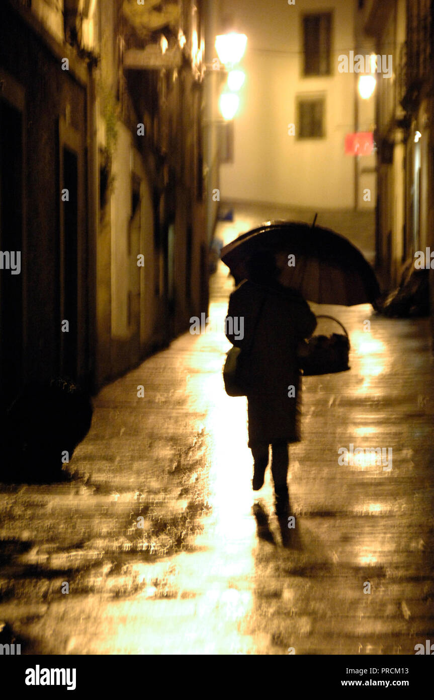 Santiago de Compostela, province of La Coruna, Galicia, Spain. Street of the old town, woman with umbrella. Night view. Stock Photo