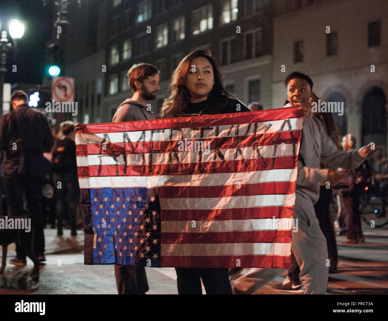 A woman carries an upside-down American flag reading 'AmeriKKKa' during protests in Oakland against the election of Donald Trump on Nov. 9, 2016. Stock Photo