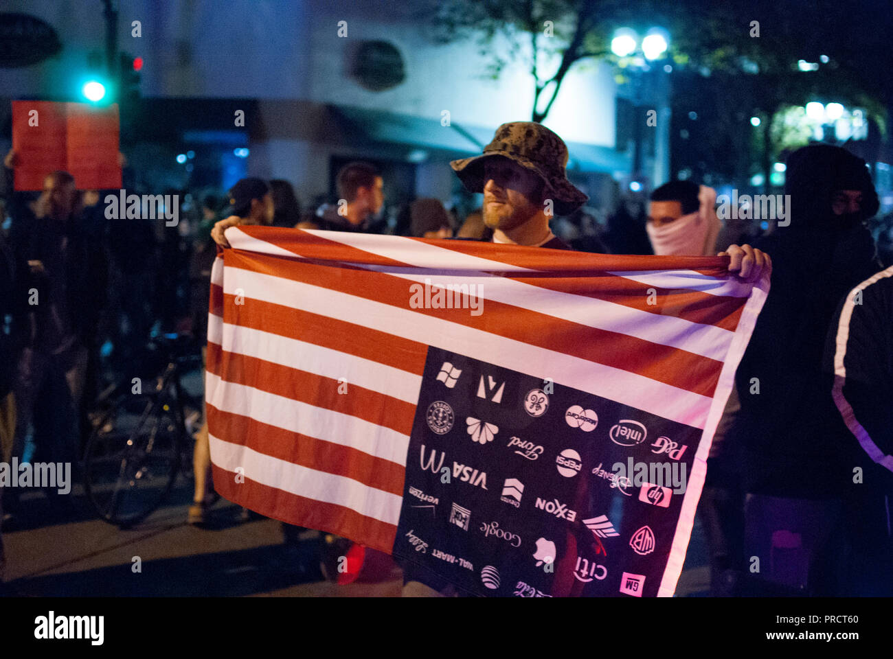 A protester holds an upside down American flag with corporate logos during protests against the election of President Donald Trump on Nov. 9, 2016. Stock Photo