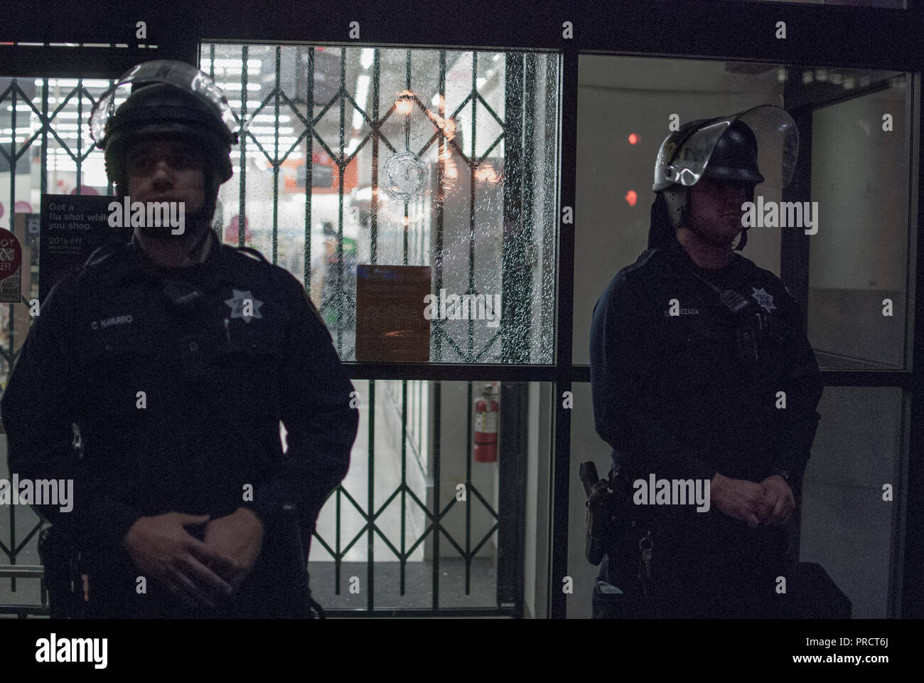 Oakland police officers stand in front of a broken window at a CVS store downtown during protests over the election of President Donald Trump. Stock Photo