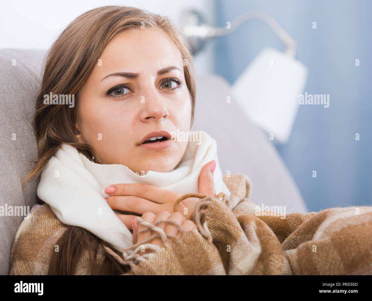 Sick girl with scarf on neck lying on sofa under blanket Stock Photo