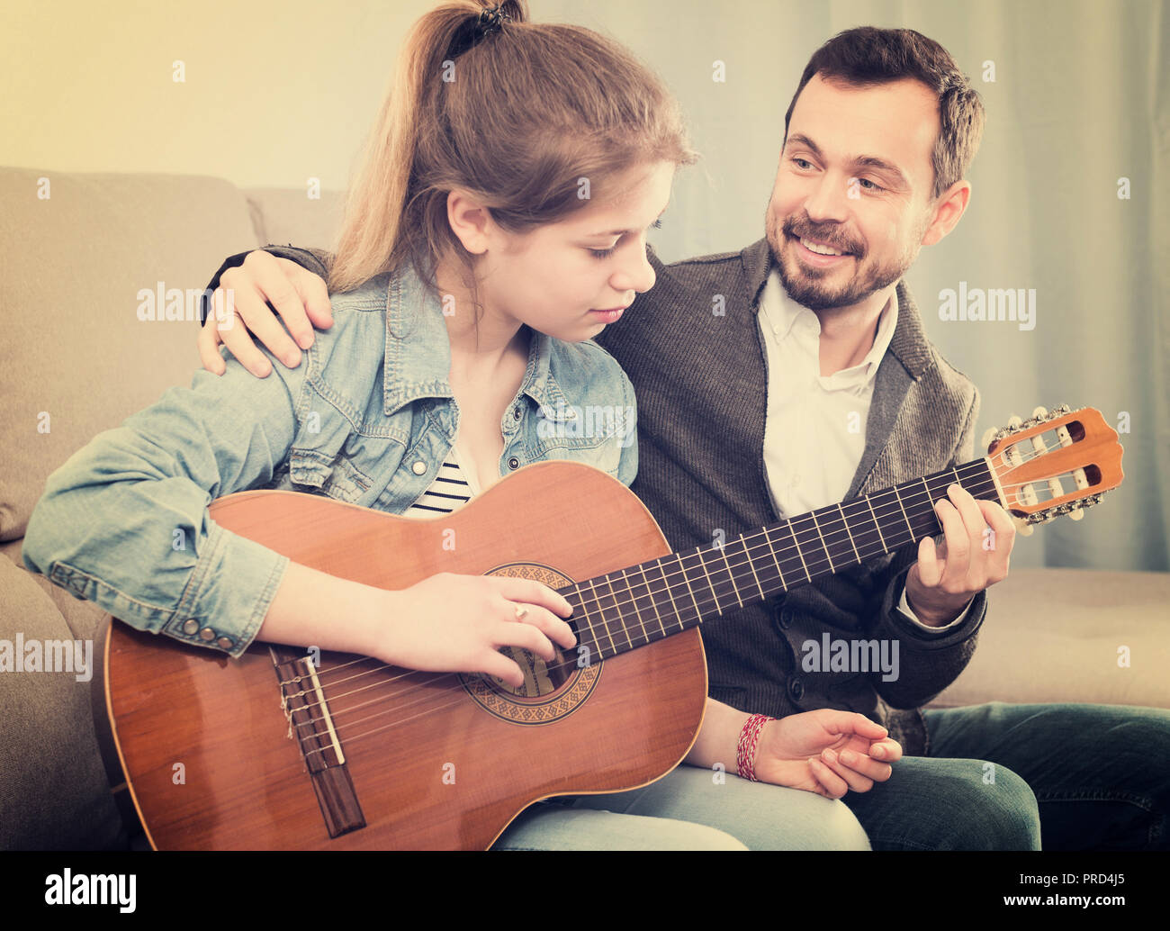 Happy adult guitar tutor helping teenage client to learn instrument ...