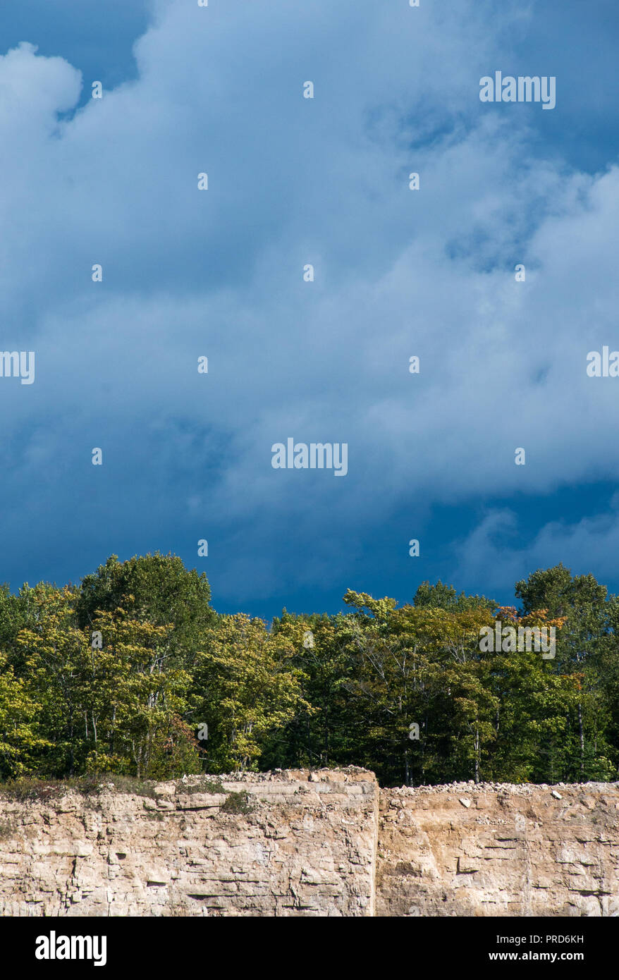 Dark sky and clouds background with trees and limestone quarry rock face in autumn landscape Stock Photo