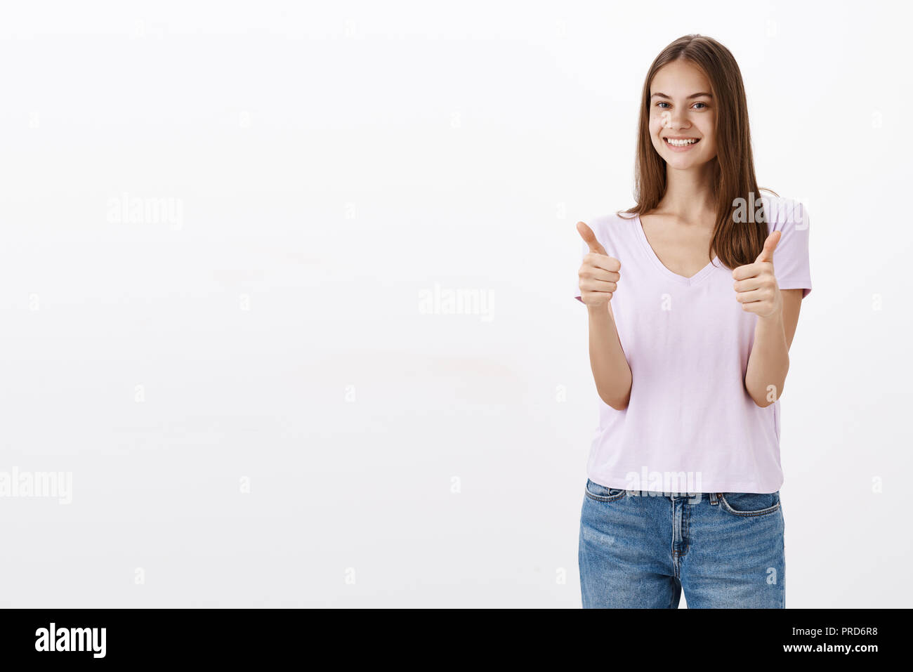 Yes I recommend you. Portrait of satisfied happy and pleased good-looking friendly woman in casual blouse and jeans showing thumbs up and smiling broadly being pleased with good quality of product Stock Photo