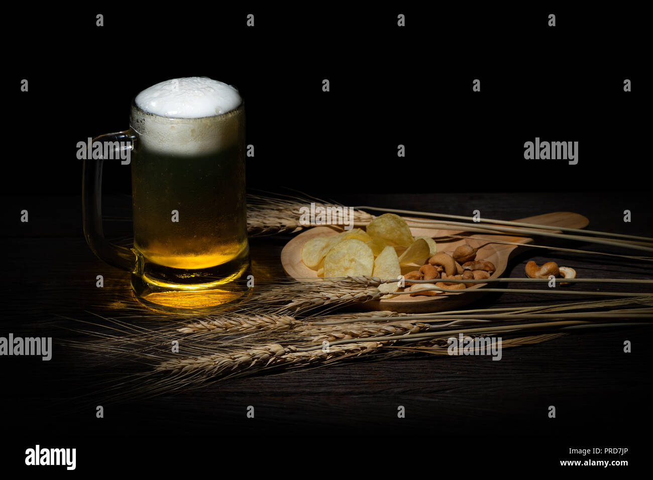 A mug of cold beer with foam on the top serve with potato chips and cashew nuts Stock Photo