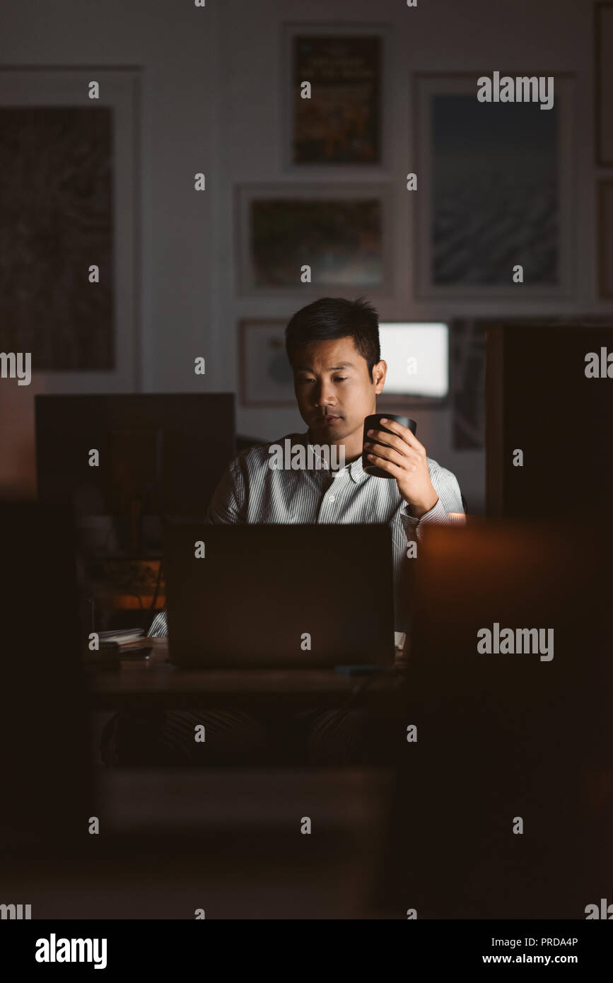 Asian businessman drinking coffee while working in a dark office Stock Photo