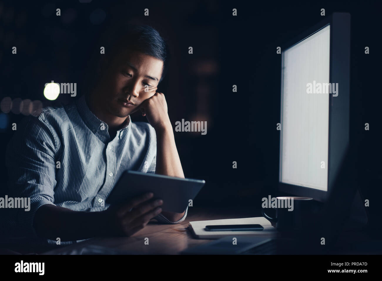 Tired Asian businessman working online in a dark office Stock Photo
