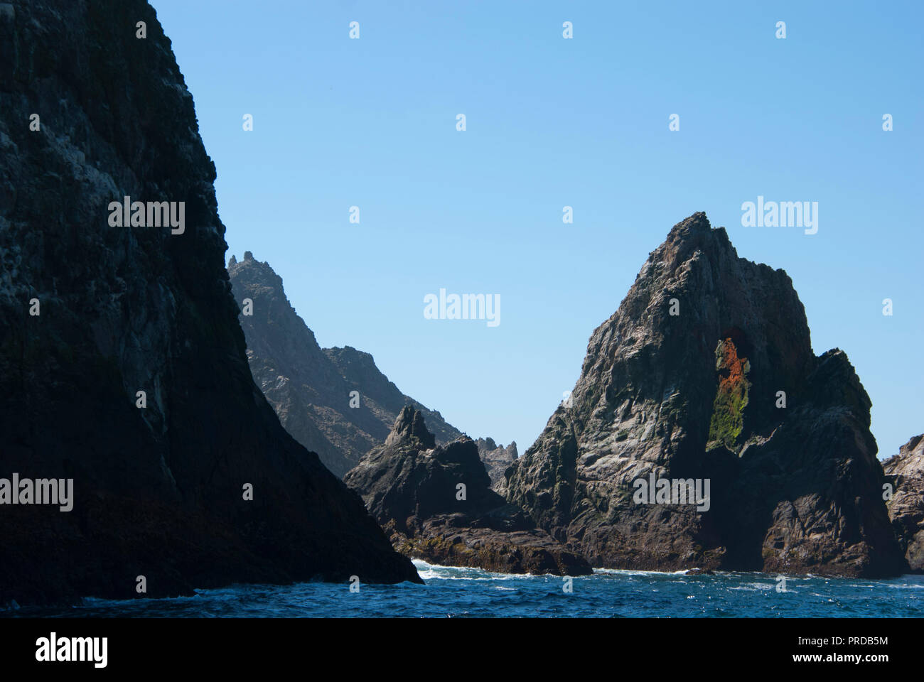 A rock arch on Southeast Farallon Island from behind a larger rock on a clear day. Stock Photo