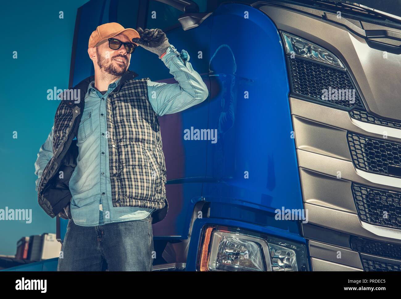 Semi Truck Driver and Hit Modern Vehicle. Happy Caucasian Trucker in His 30s. Transportation Industry. Stock Photo