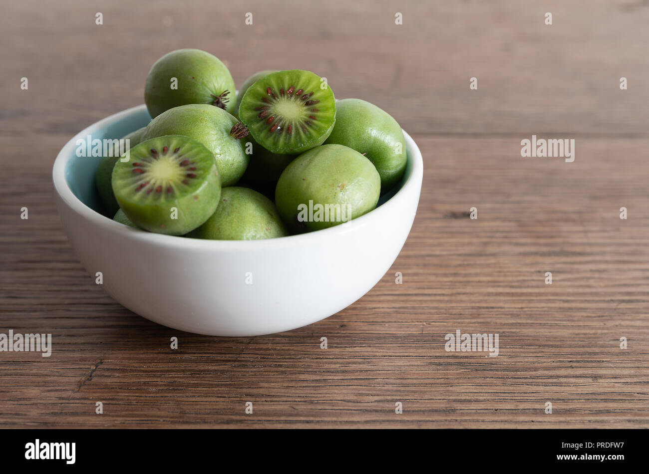 hardy kiwi fruits or kiwi berry in ceramic bowl on table Stock Photo