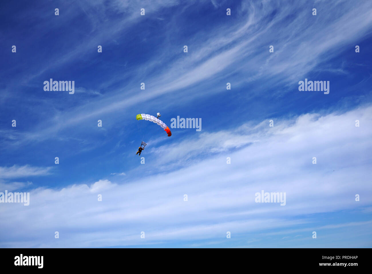 Bright color parachute canopy and tandem's skydivers against the background of a dazzling white clouds and a blue sky. Tandem master with passenger is Stock Photo