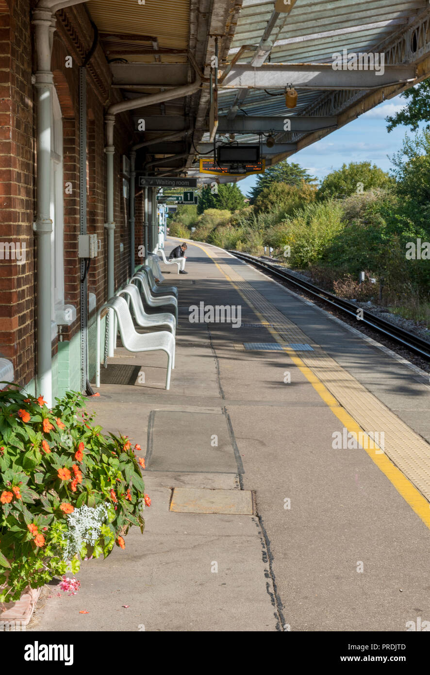 man sitting on a bench at Barnham railway station in West Sussex. Stock Photo
