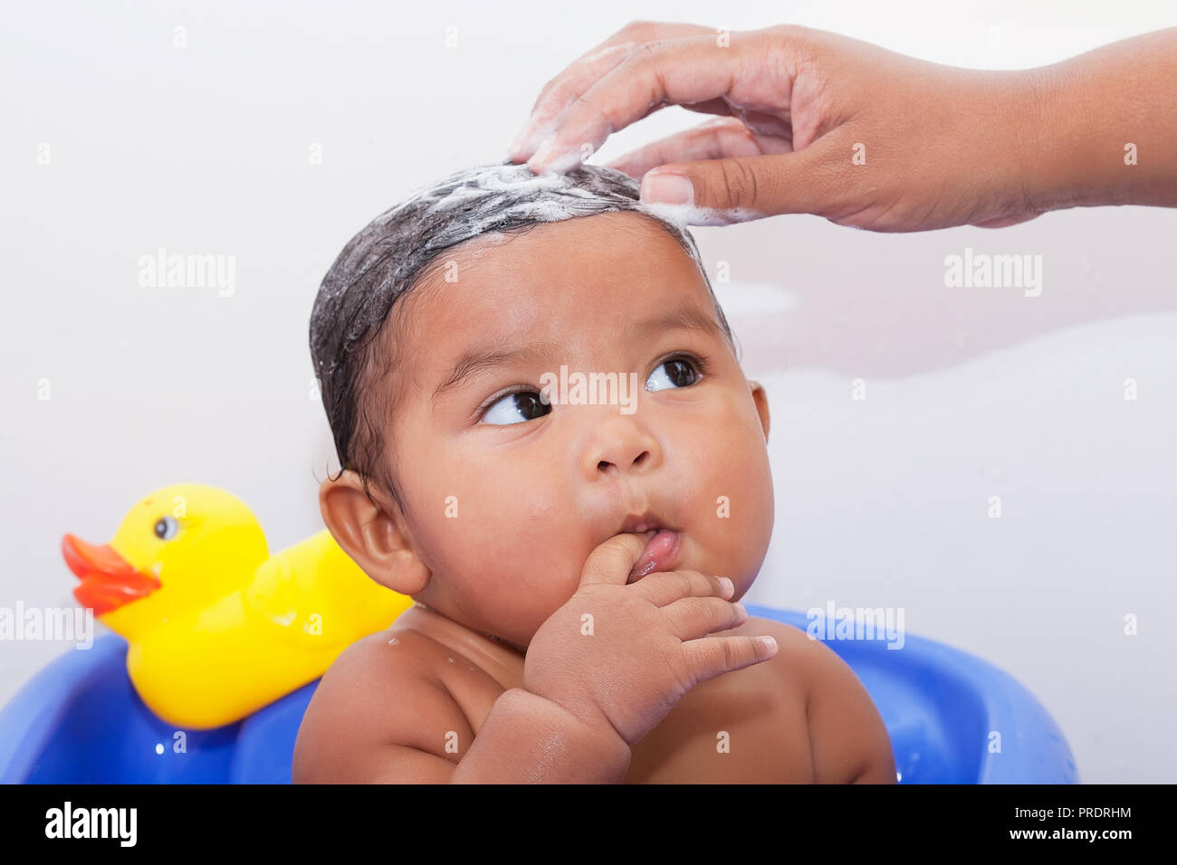 Moms hand washing the baby's head with shampoo and baby staring with