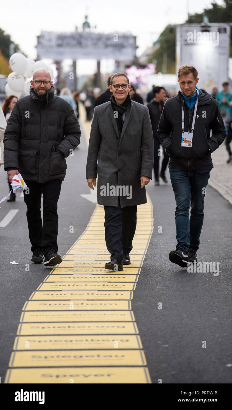 01 October 2018, Berlin: 01 October 2018, Germany, Berlin: Michael Mueller (C, SPD), Governing Mayor of Berlin and current President of the Bundesrat, is taking a tour of the Buergerfestmeile at the start of the celebrations for German Unification Day together with Moritz van Duelmen (L), Managing Director of Kulturprojekte Berlin GmbH, and Julian Mieth (R), Deputy Senate Spokesman. He goes on the tape of unity with the place names of all 11 040 German cities and municipalities. This year, Berlin is hosting the central celebration of the anniversary of German unity. The citizens' festival arou Stock Photo