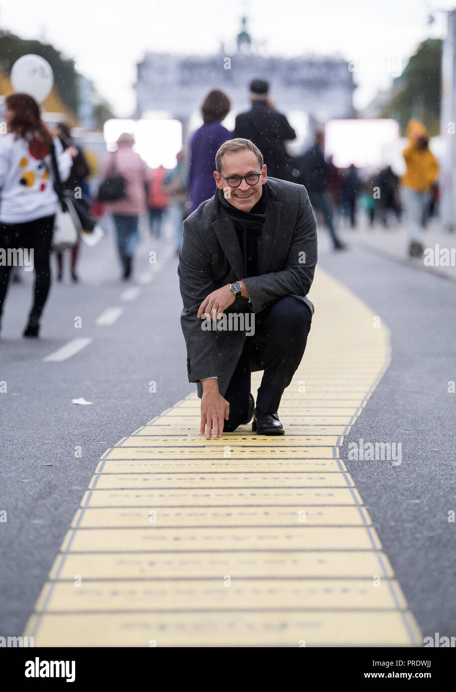 01 October 2018, Berlin: 01 October 2018, Germany, Berlin: Michael Mueller (C, SPD), Governing Mayor of Berlin and current President of the Bundesrat, is taking a tour of the Buergerfestmeile at the start of the celebrations for German Unification Day together with Moritz van Duelmen (L), Managing Director of Kulturprojekte Berlin GmbH, and Julian Mieth (R), Deputy Senate Spokesman. He points to the band of unity with the place names of all 11 040 German cities and municipalities. This year, Berlin is hosting the central celebration of the anniversary of German unity. The citizens' festival ar Stock Photo