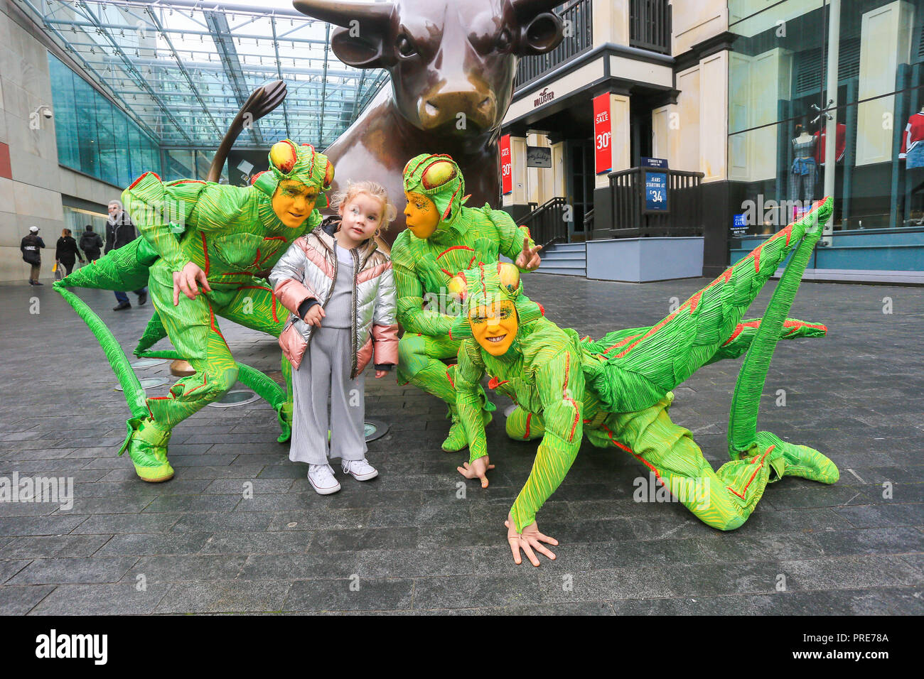 Birmingham, UK. 2nd October, 2018. Three of the cast of crickets in Cirque de Soleil's OVO show arrive in Birmingham Bull Ring ahead of their premiere performance on Wednesday 3rd October in The Arena, Birmingham. 4 year-old Isla from Birmingham is cuaght up in the theatrics. The production of one of the world's most creative and skilful circuses runs from 3rd - 7th October 2018. Peter Lopeman/Alamy Live News Stock Photo