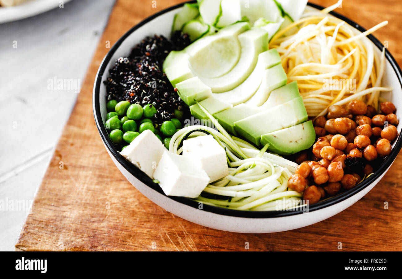 Vegetarian buddha bowl. Clean healthy food concept. Spiralized vegetables, avocado, green peas, cucumber, chickpeas and black quinoa on white wooden t Stock Photo