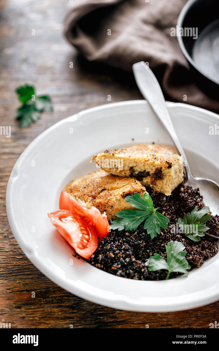 Dinner table. Fried prunes oat cutlets with black quinoa in plate on wooden table Stock Photo