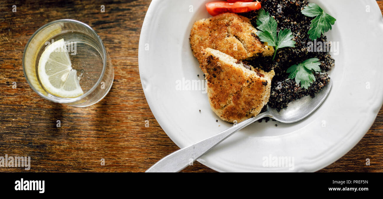 Dinner table. Fried prunes oat cutlets with black quinoa in plate on wooden table top view Stock Photo