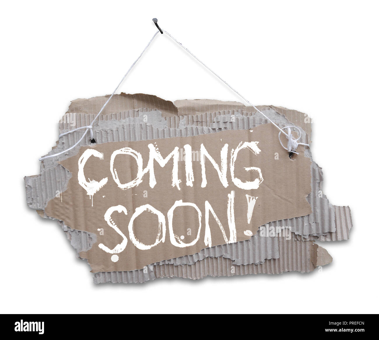 Cardboard sign with message COMING SOON. Ripped corrugated paper on a rope and with handwritten inscription COMING SOON. Isolated on white background. Stock Photo