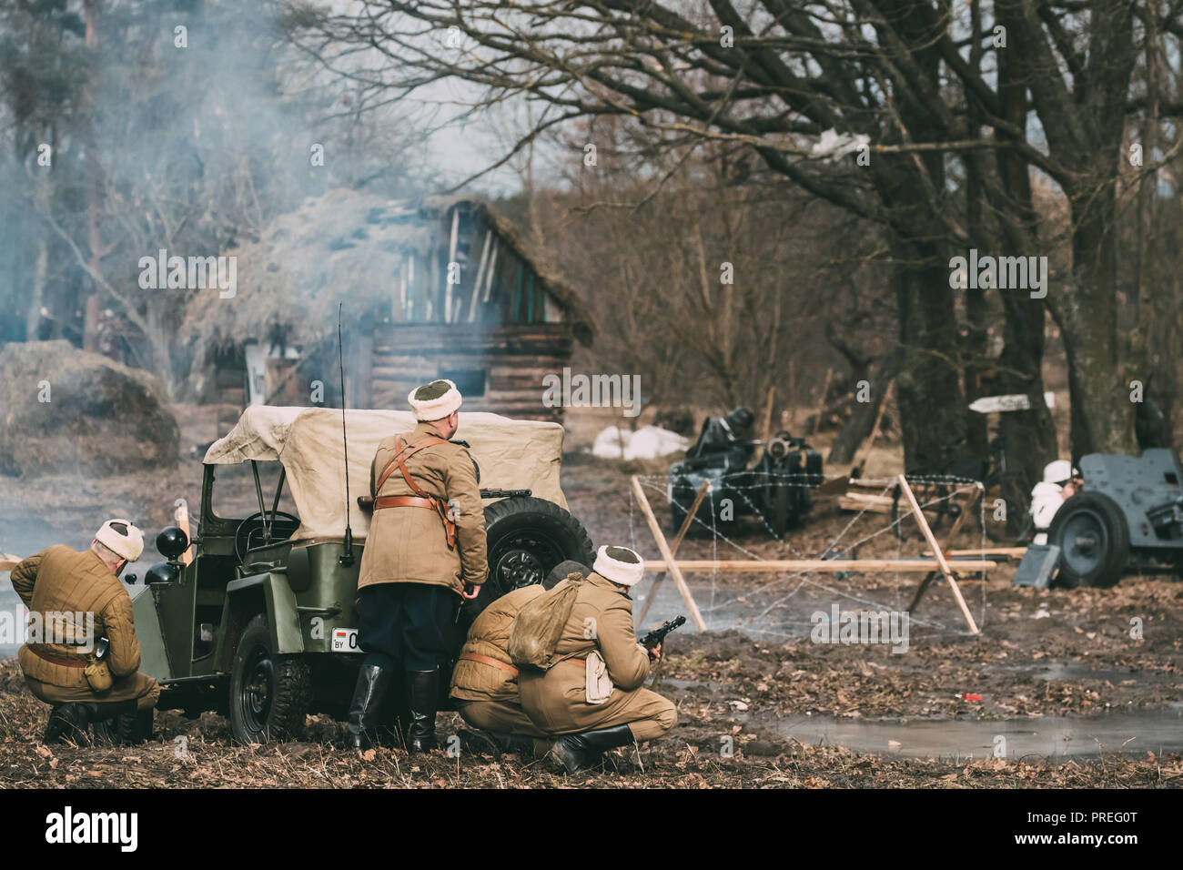 Group Of Reenactors Dressed As Russian Soviet Red Army Soldiers Of World War II Go On Offensive Under Cover Of Soviet Scout Car. Historical Reenactmen Stock Photo