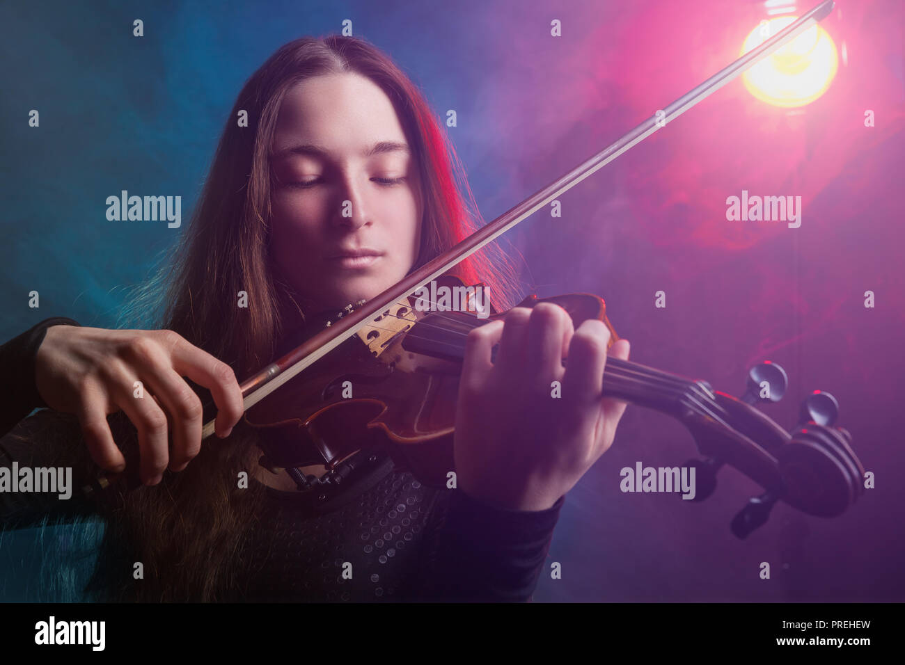 Beautiful girl playing the violin. Multicolored fog in the background. Studio shot Stock Photo