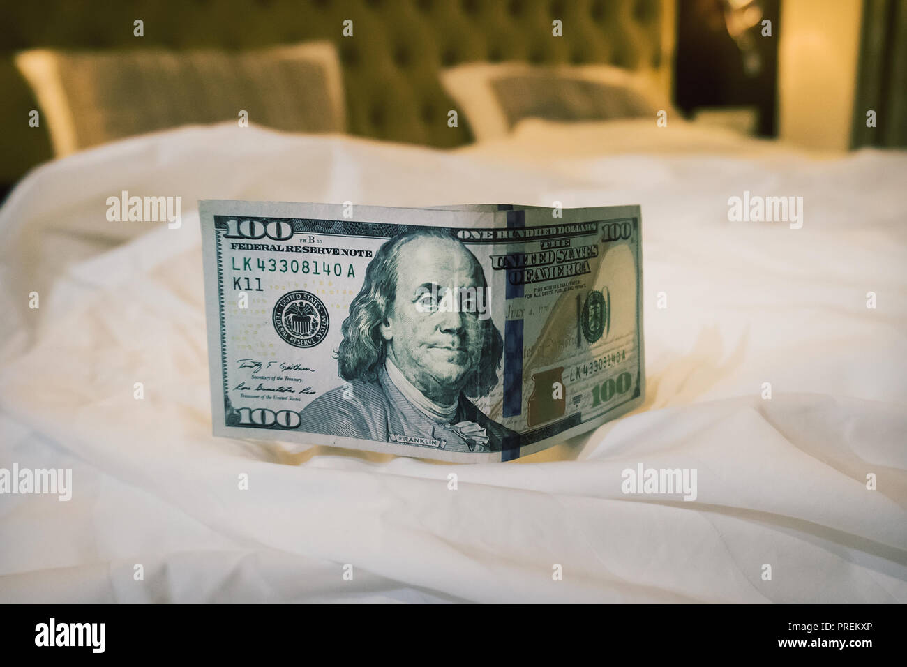 a good tip, some hundred dollars on the table on a blurred bed background. Tips at the bed for the housekeeper in hotel. Stock Photo