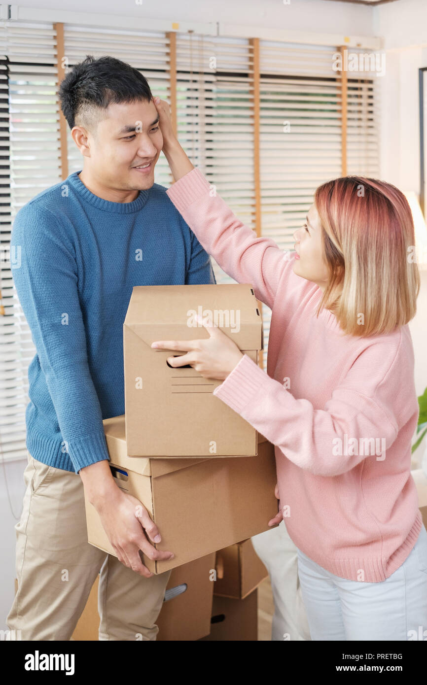 Happy asian couple carry cardboard boxes while moving to new house in living room.unpacking for new home.woman wipe the sweat her husband Stock Photo