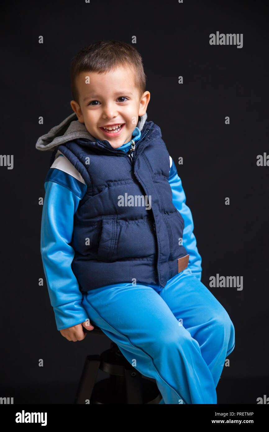 Portrait of little boy laughing while sitting on a black stool, isolated on black background Stock Photo