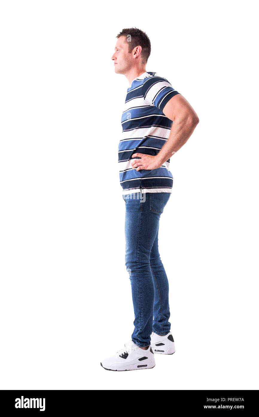 Side view of confident young casual man with arms on waist looking away ...