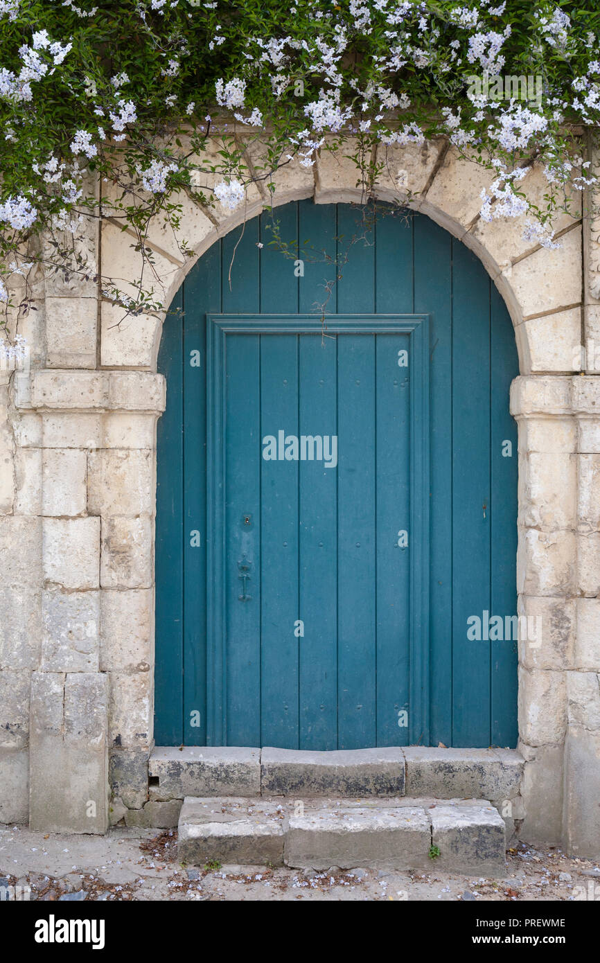 Rustic blue wooden door with white flowers above. Stock Photo