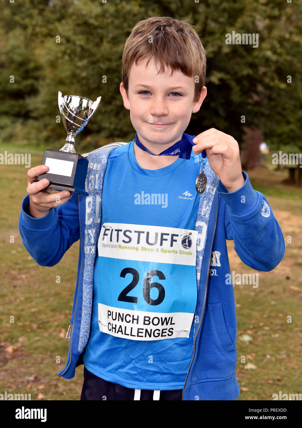 8 year old boy proudly displaying his medal and cup after winning a 1KM cross country running race, Hindhead, Surrey, UK. Sunday 30 September 2018. Stock Photo