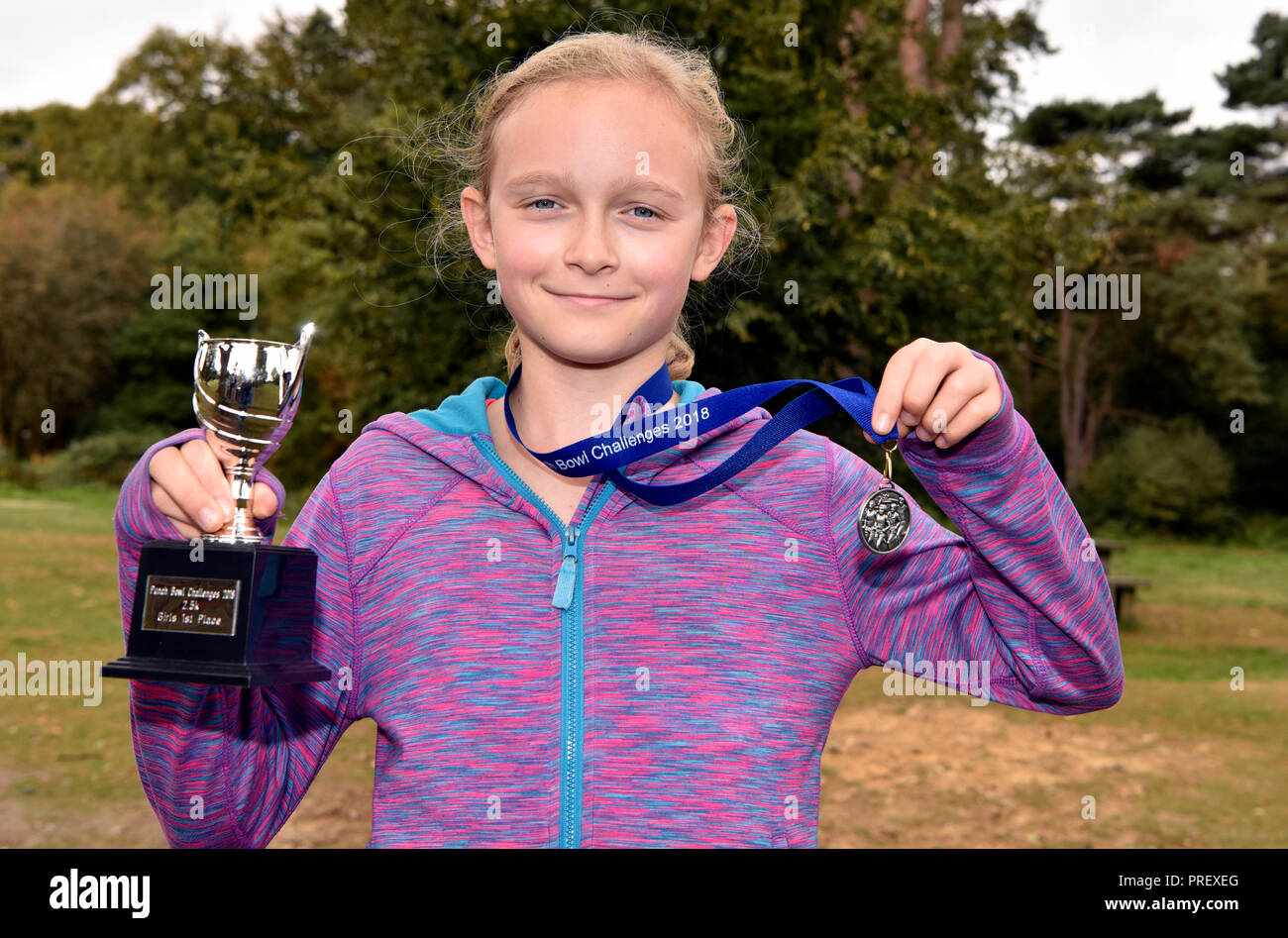 10 year old girl proudly displaying her medal and cup after becoming the first girl to cross the finish line in a 2.5KM cross country running race... Stock Photo