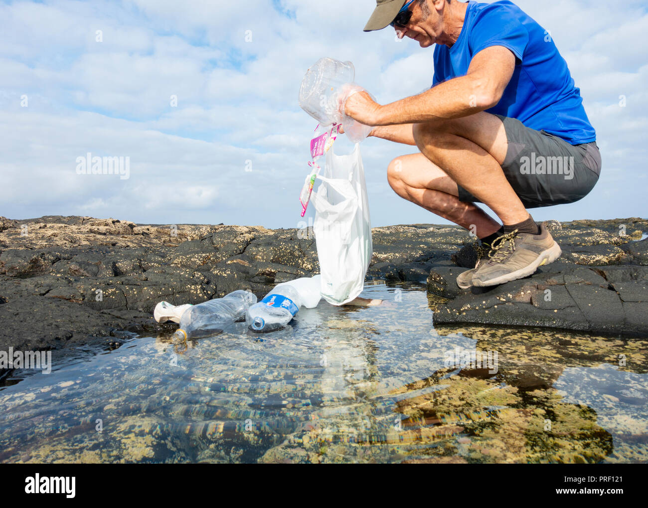 A Plogger/jogger collects plastic rubbish from beach rockpool during his morning run Stock Photo