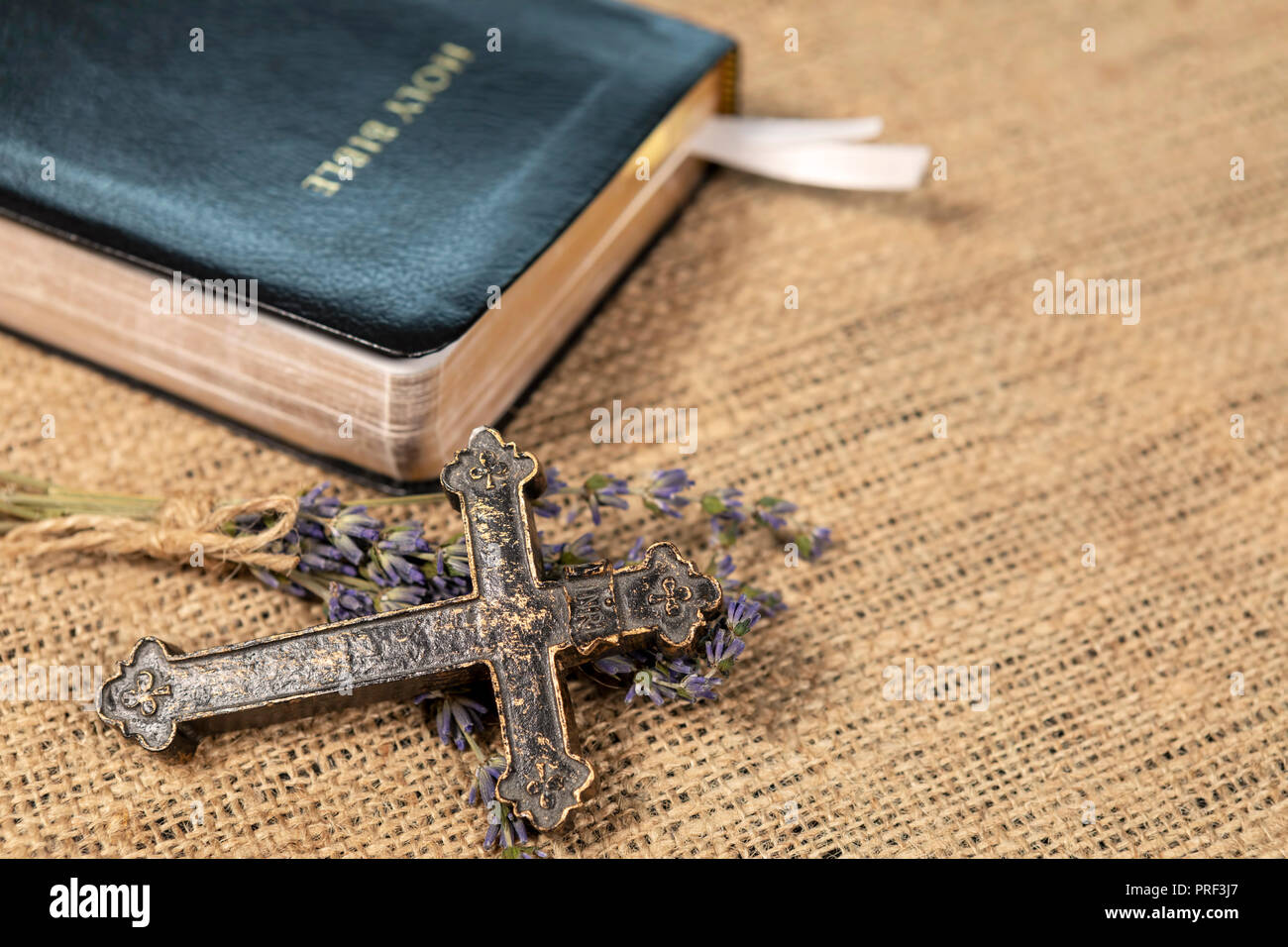 Closeup of metalic Christian cross on lavanda flowers next to Holy Bible on textile background. Stock Photo