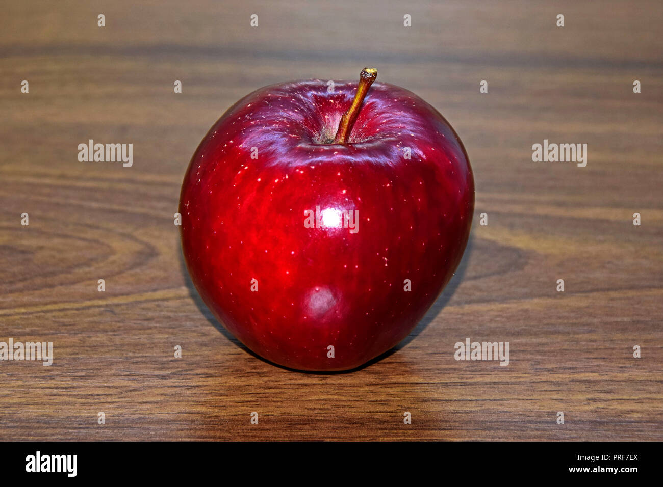 A shiny , ripe dark red apple with white spots lain on brown wooden desktop, in lateral close-up view Stock Photo