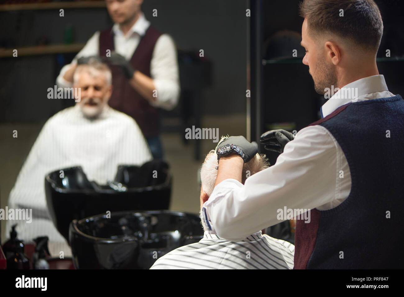 Professional barber in white shirt, vest and black gloves grooming and