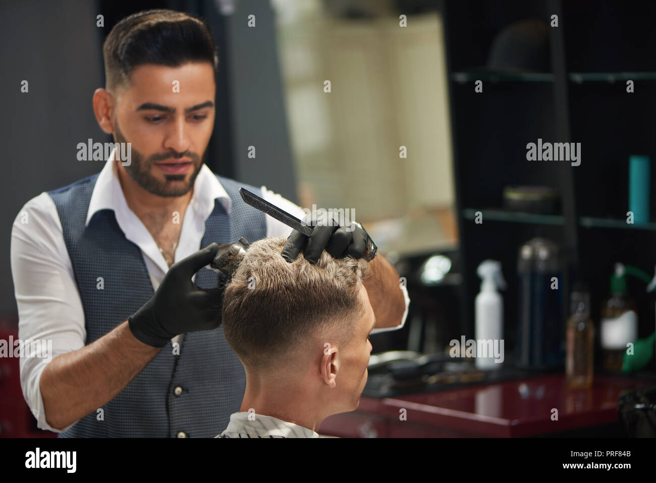 Concentrated Barber Looking At Client And Trimming Haircut Of