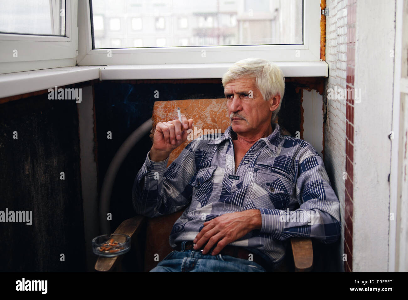 portrait of a gray-haired man 60 years old. A man sits in a chair and smokes a cigarette Stock Photo