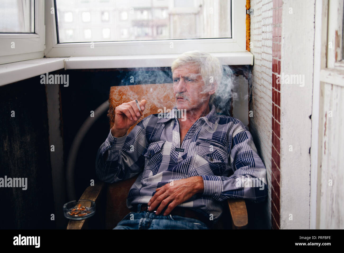 portrait of a gray-haired man 60 years old. A man sits in a chair and smokes a cigarette Stock Photo